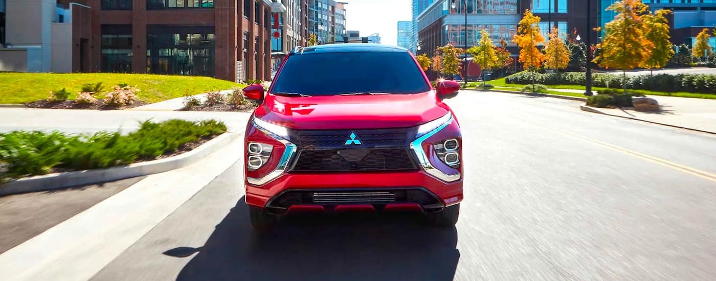 A red 2023 Mitsubishi Eclipse Cross driving through the city to a used Mitsubishi dealer.