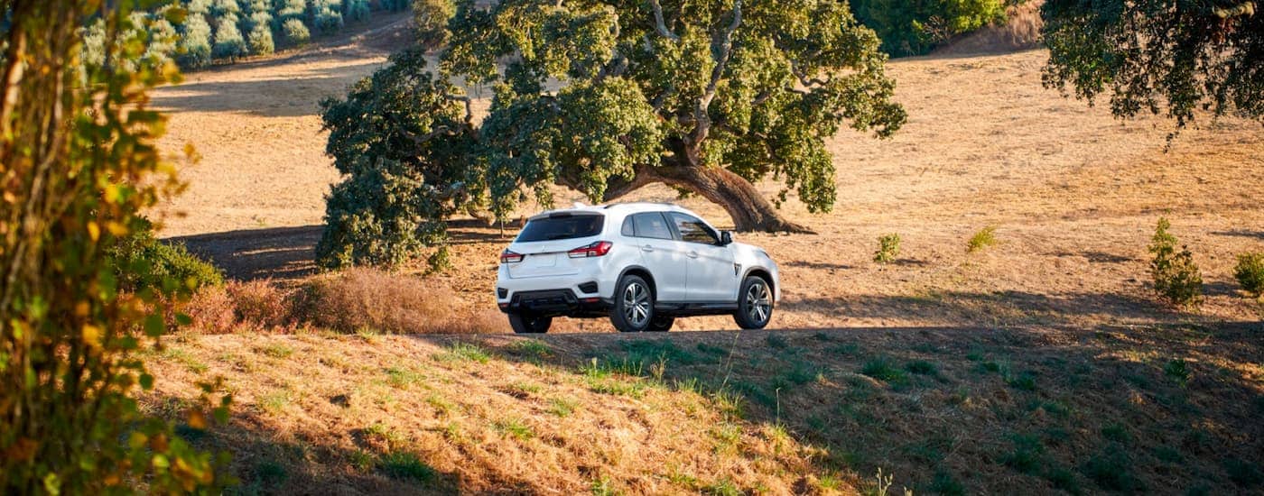 A white 2024 Mitsubishi Outlander Sport driving on a winding road through a field.