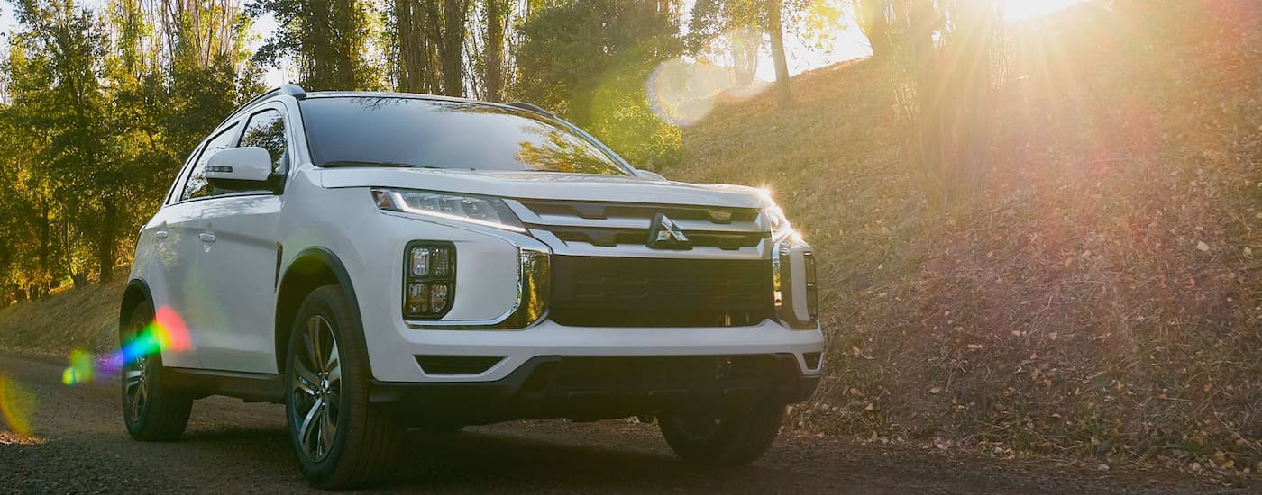 A white 2024 Mitsubishi Outlander Sport driving on a road lined with trees.