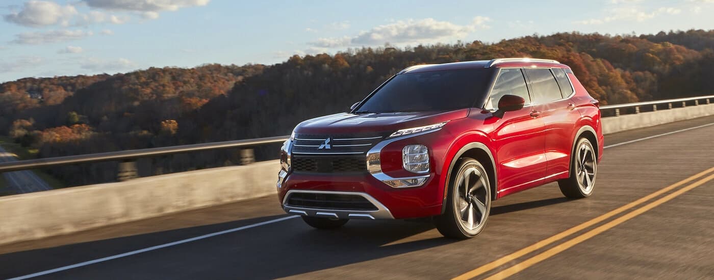 A red 2022 Mitsubishi Outlander driving on a bridge over a river.