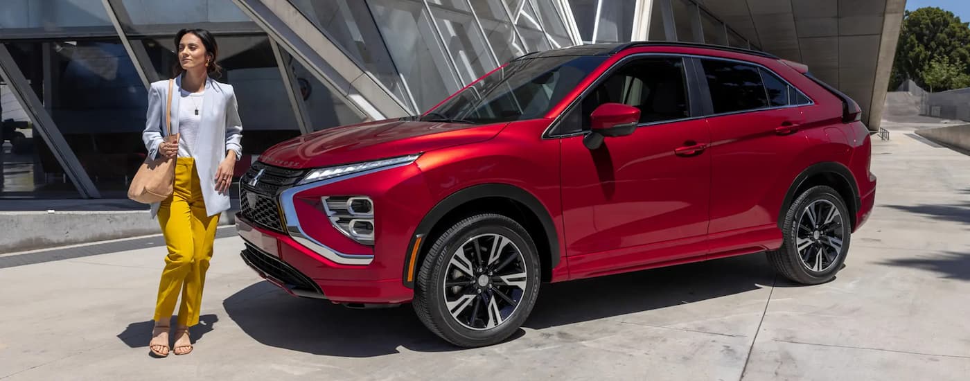 A red 2023 Mitsubishi Eclipse Cross parked near a large glass building as a woman walks by.