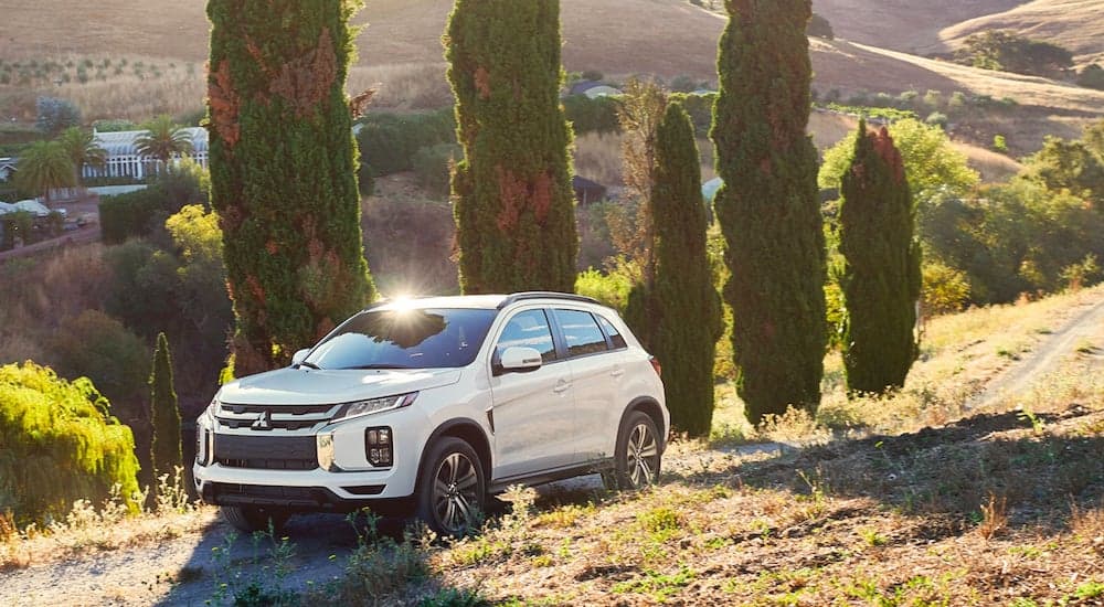 A white 2023 Mitsubishi Outlander Sport parked on a grassy hill near cypress trees.