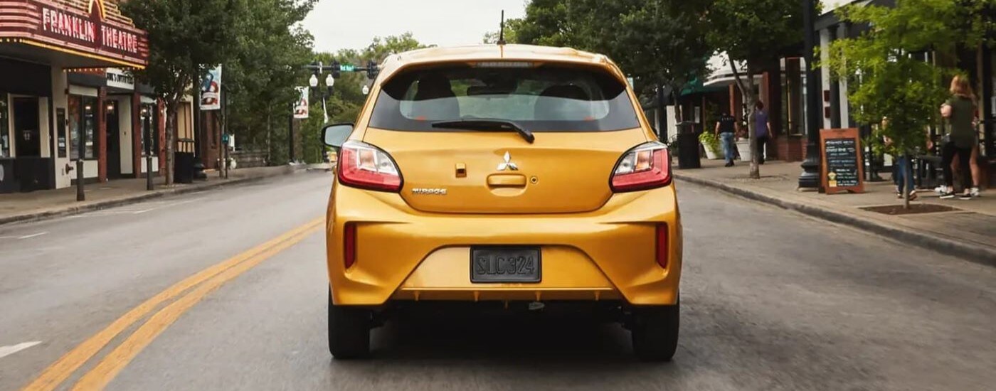 A yellow 2023 Mitsubishi Mirage G4 driving on a downtown city street.