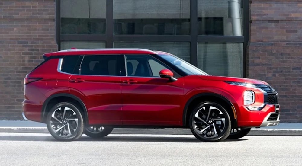 A red 2024 Mitsubishi Outlander is shown from the side on a city street.