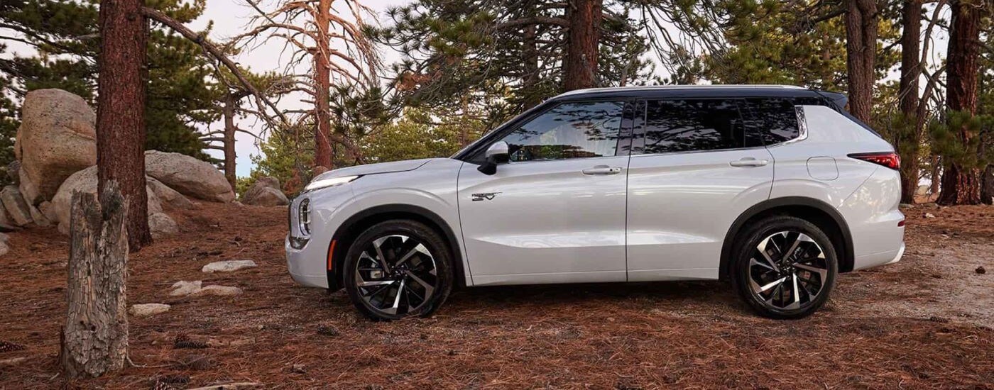 A white 2024 Mitsubishi Outlander angled left and parked off-road in a forest.