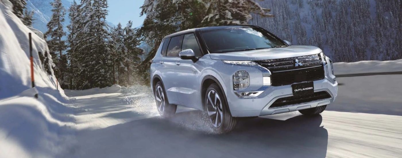 A white 2024 Mitsubishi Outlander driving down a snowy road.