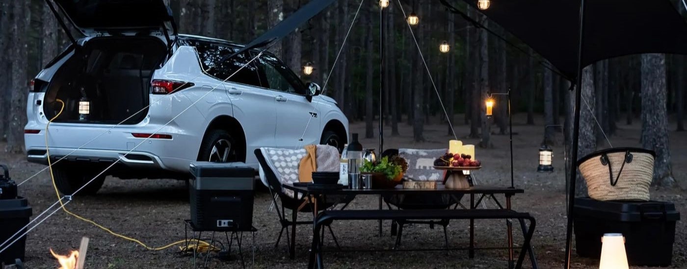 A rear view of a white 2024 Mitsubishi Outlander with an open hatchback parked at a campsite.