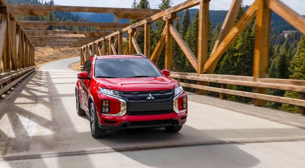 A red 2023 Mitsubishi Outlander Sport driving over a wooden bridge in the mountains
