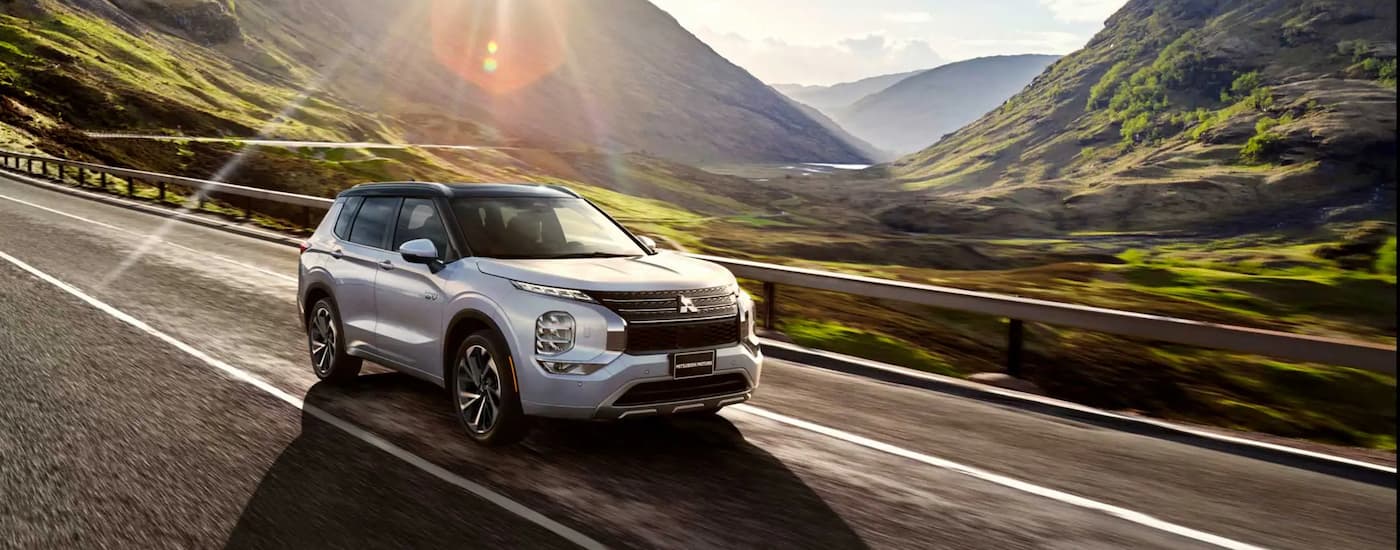 A silver 2023 Mitsubishi Outlander PHEV driving on an open road with a mountain view.