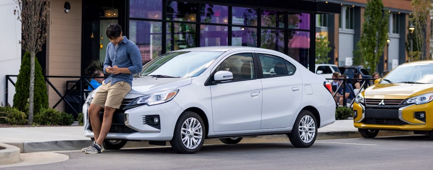 A man leaning against the hood of his white 2022 Mitsubishi Mirage G4 parked on a city street.