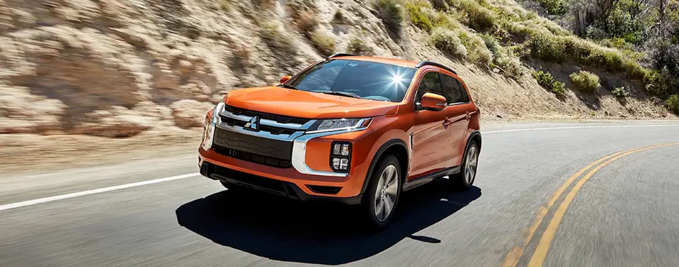 An orange 2020 Mitsubishi Outlander Sport driving on a winding road.