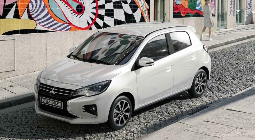 A white 2024 Mitsubishi Mirage is shown parked near graffiti on a wall after visiting a Mitsubishi dealer near Springfield.