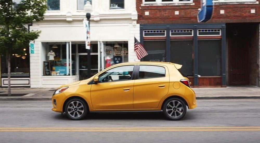 A yellow 2023 Mitsubishi Mirage G4 driving past city storefronts.