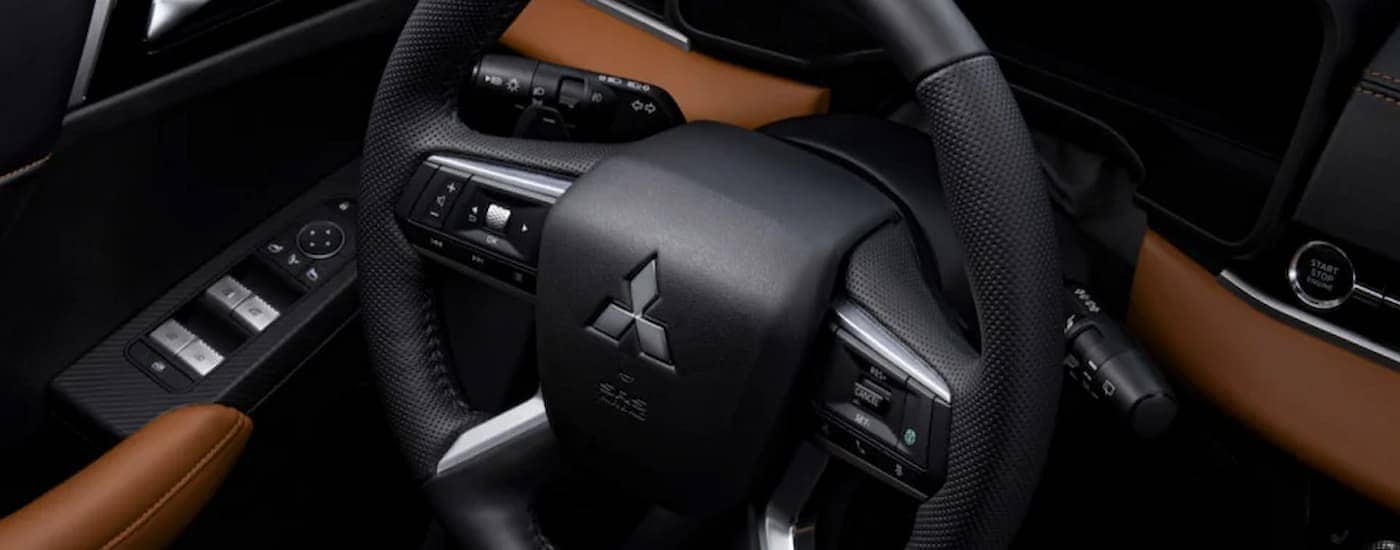 A close up of the steering wheel and black and brown interior of a 2023 Mitsubishi Outlander for sale.