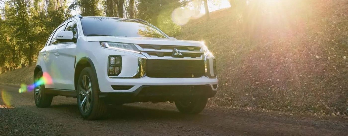 A white 2023 Mitsubishi Outlander Sport driving on a sunny trail after leaving a Mitsubishi dealer in Marlow Heights.