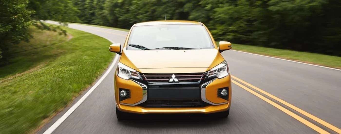 A yellow 2024 Mitsubishi Mirage for sale is shown driving on a street.