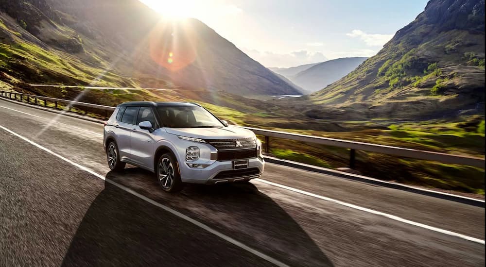 A silver 2023 Mitsubishi Outlander PHEV for sale is shown driving on a mountain highway.