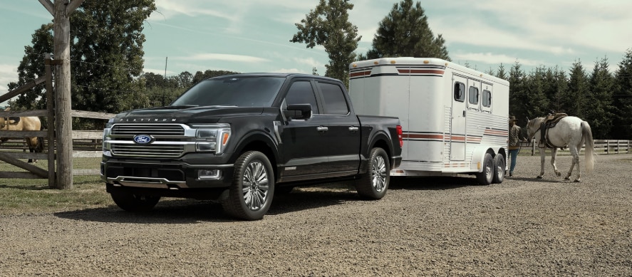 A black Ford F-150 hooked up to a white trailer on a ranch.