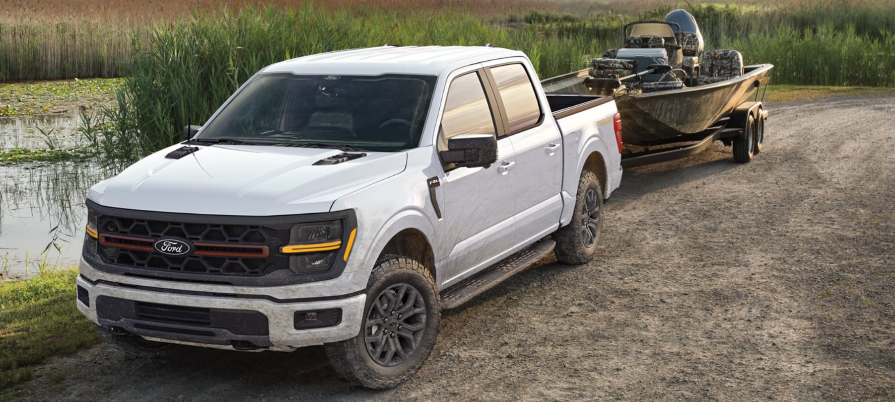 A white Ford F-150 towing a boat off-road by a swamp.