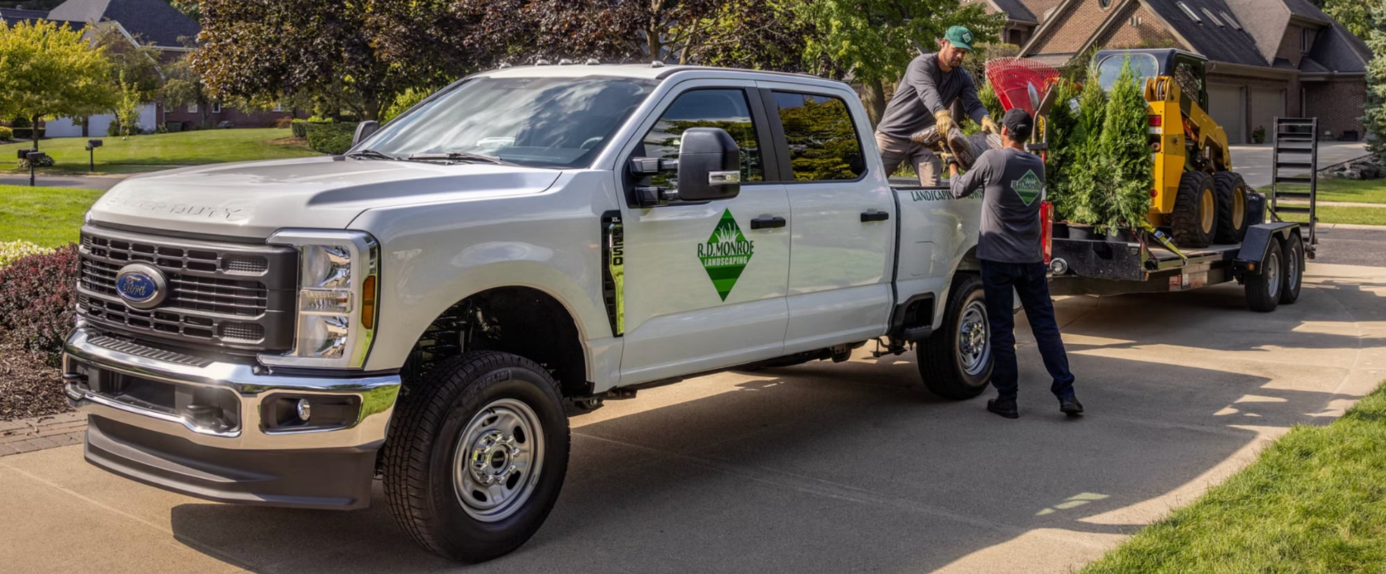 A silver heavy-duty Ford pickup being prepared to a pine tree and equipment in a driveway.