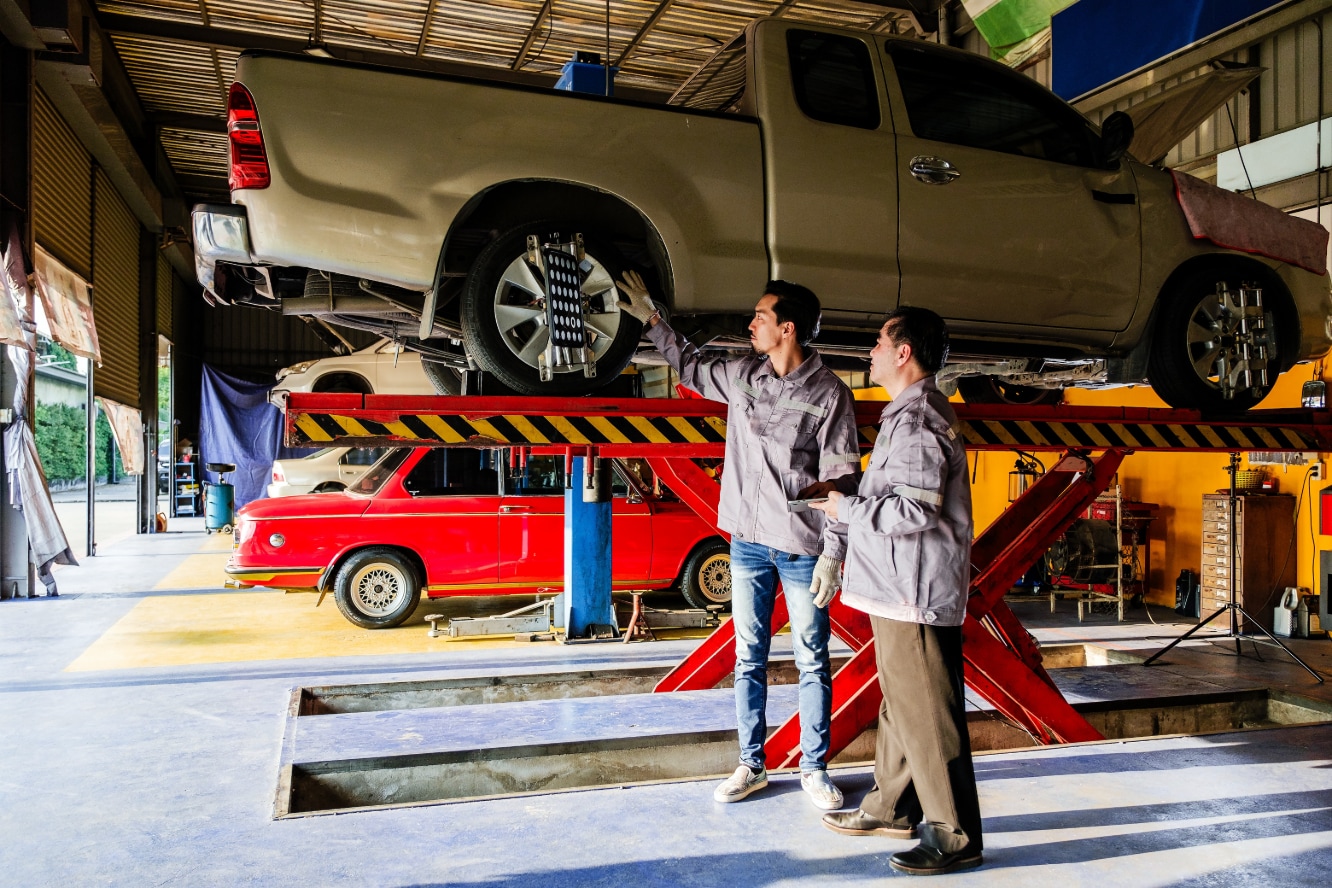 A pair of mechanics examining a raised pickup truck.