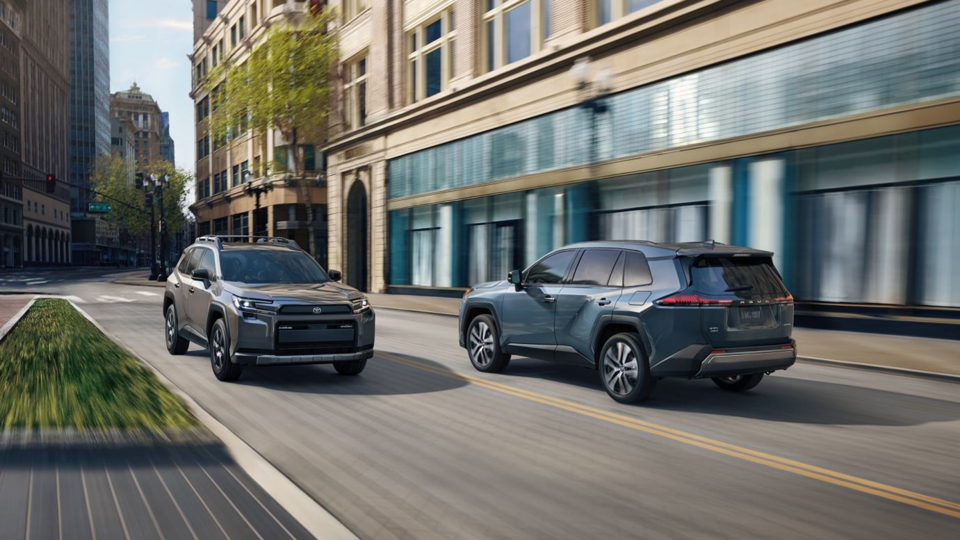 A blue and gray Toyota RAV4 driving by each other in a city.