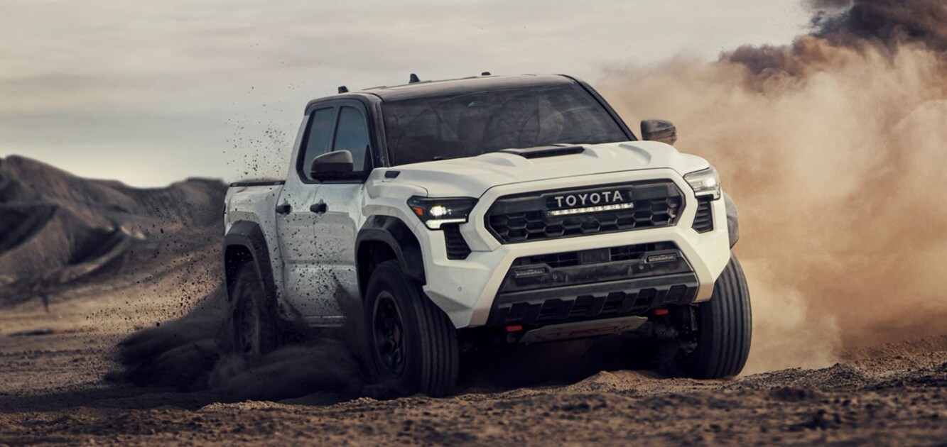 A white Toyota Tacoma driving off-road through mud and dirt.