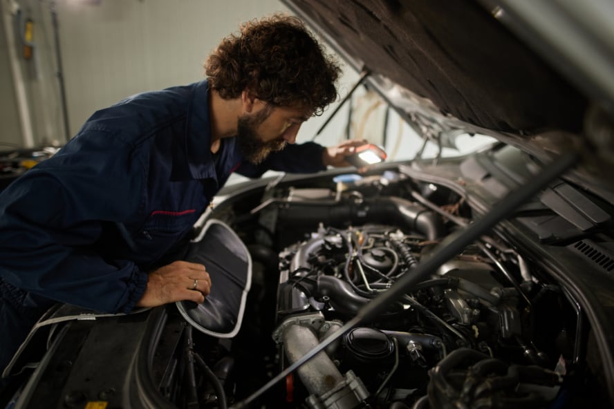 A technician examining under a vehicle's hood.