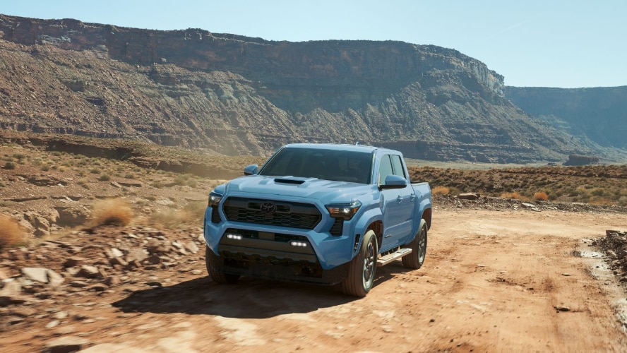 A light blue Toyota Tacoma driving on a dirt road through the desert.