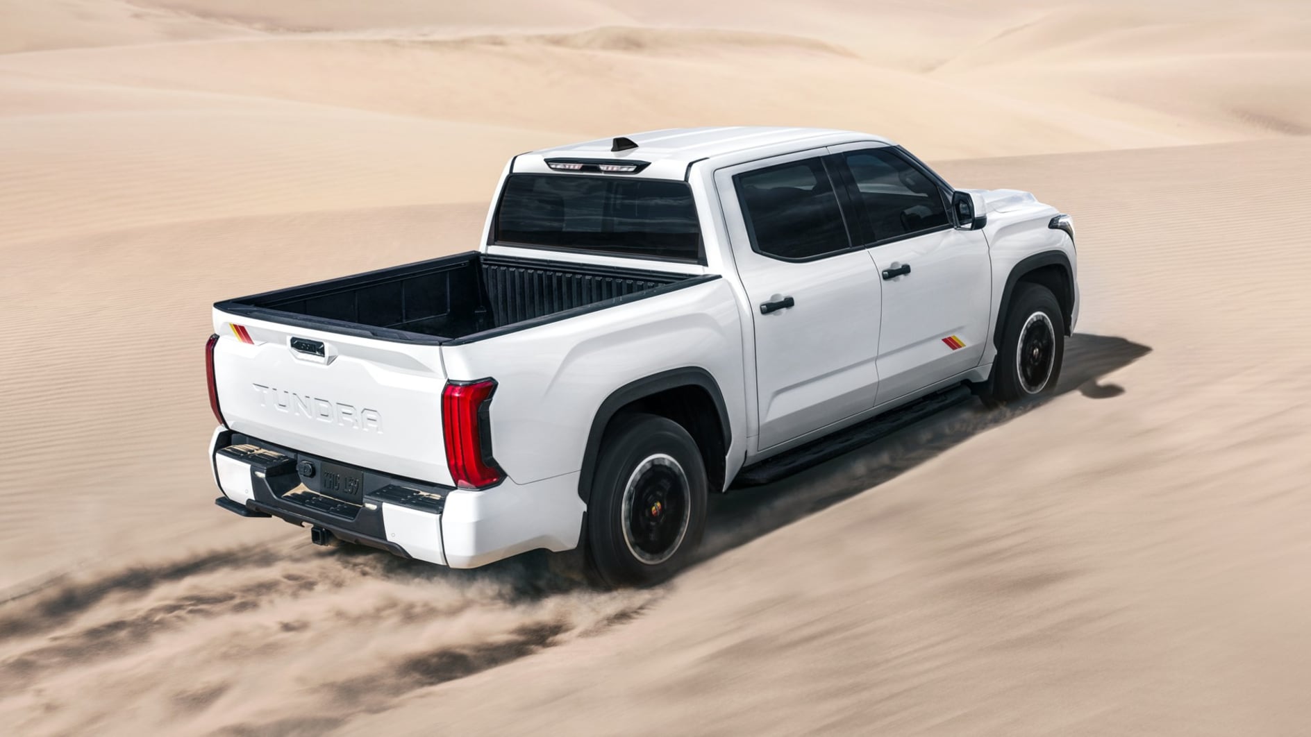 A rear view of a white Toyota Tundra driving through a desert.