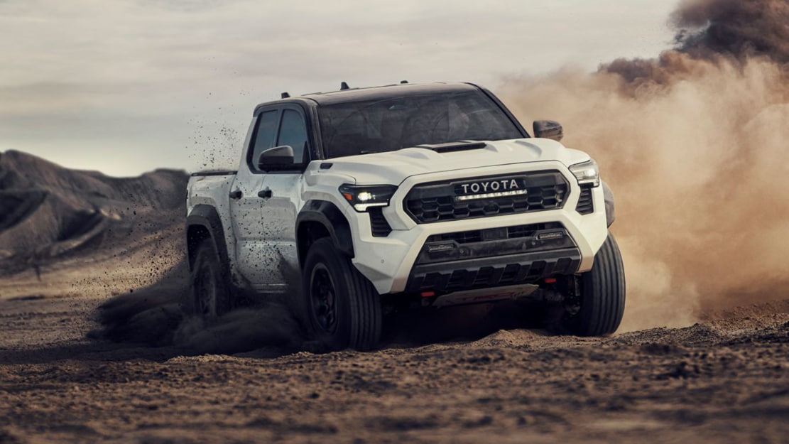 A white Toyota Tacoma driving off-road through mud and dirt.
