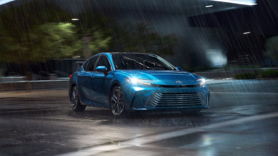 A blue Toyota Camry driving in the rain.