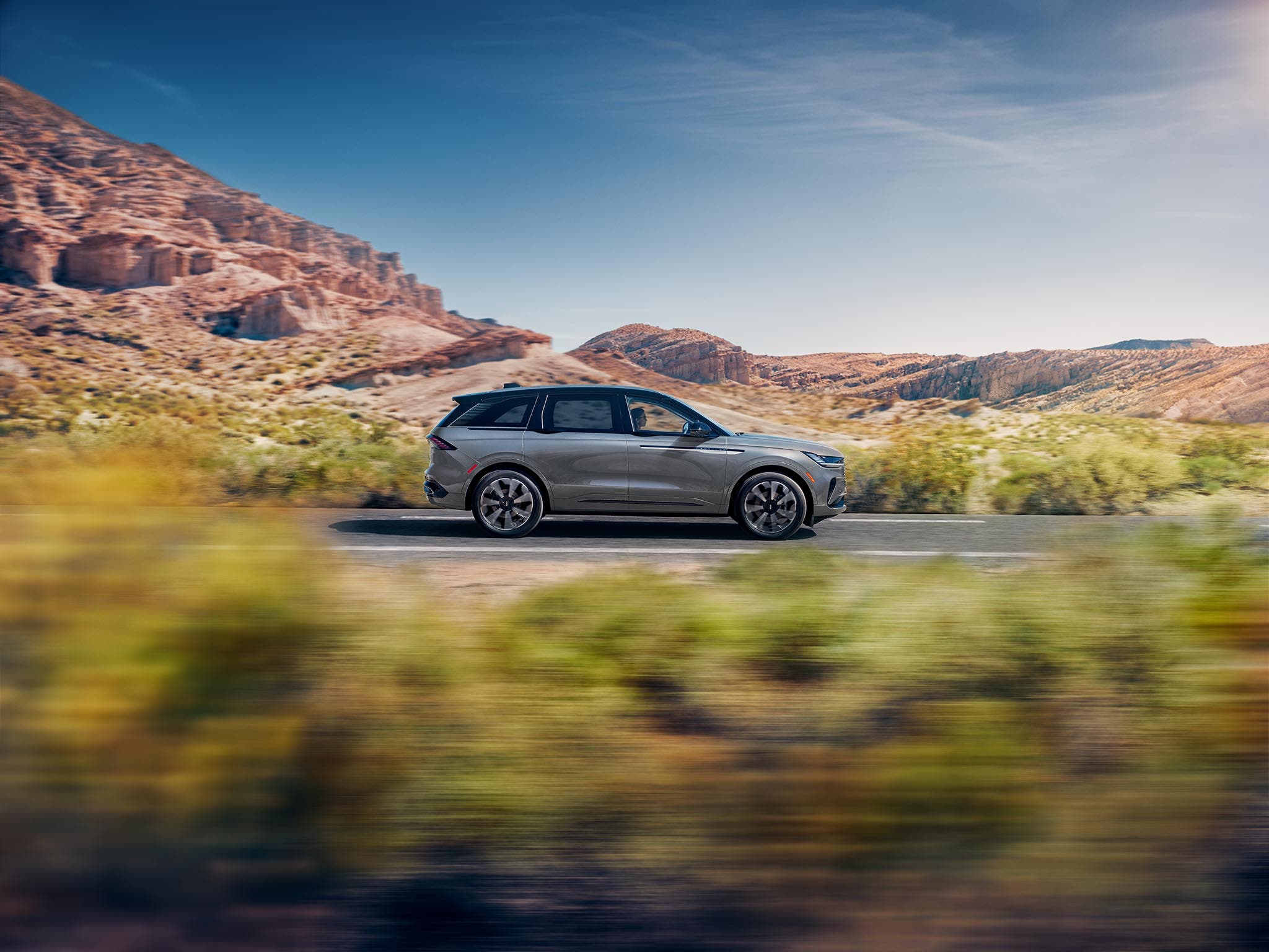 A Lincoln Nautilus Reserve Hybrid driving past a red rock canyon, the background blurred with speed