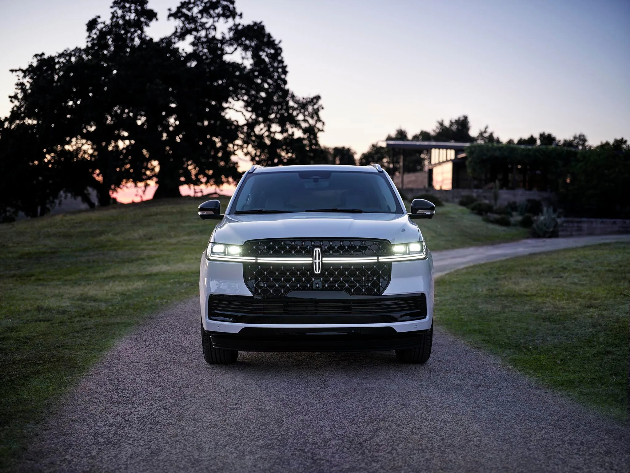 A Lincoln Navigator seen head on at dusk with its grille and headlights lit