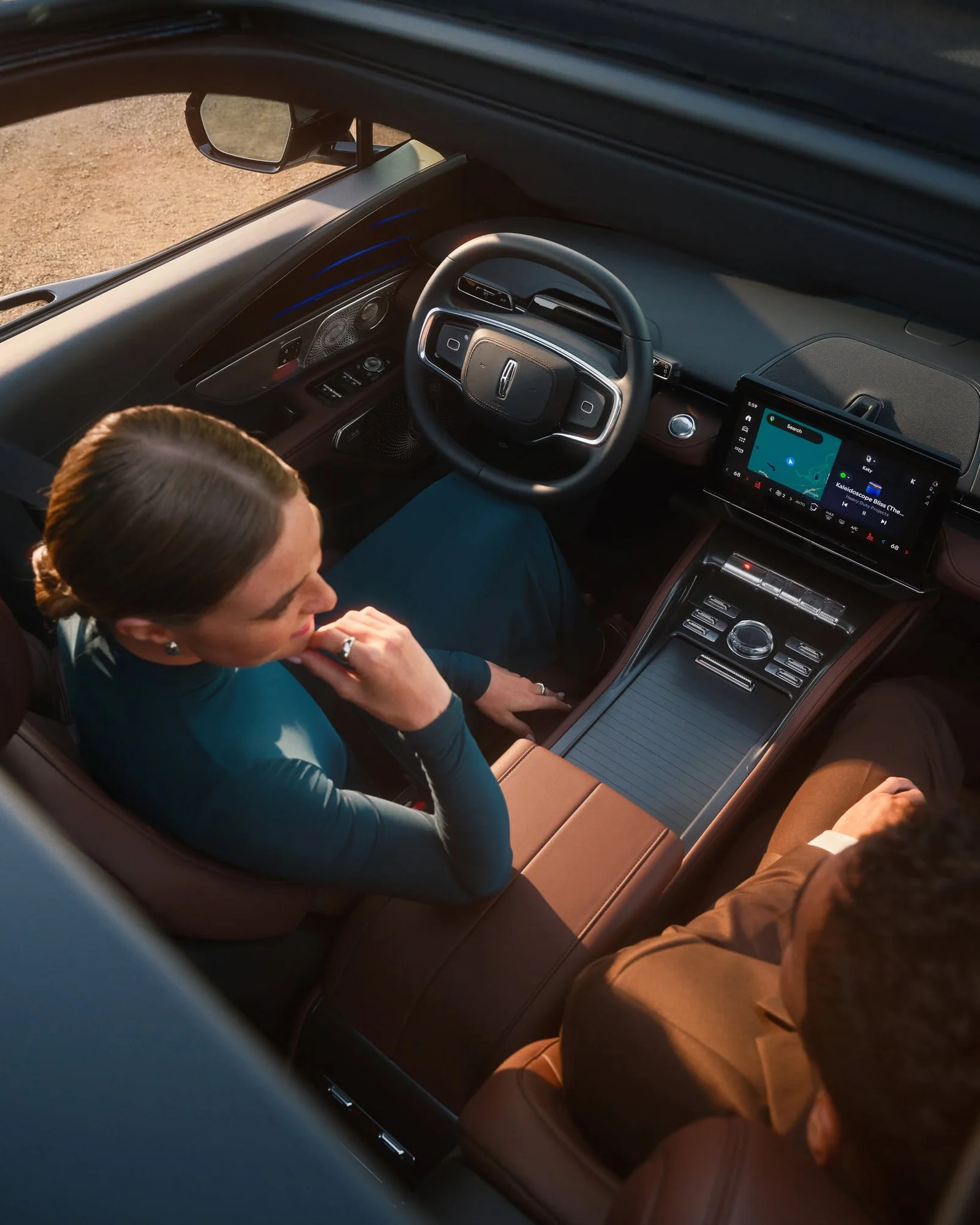 Two people sitting in the front of a Lincoln SUV, the panoramic display lit up across the dash above a tan leather console