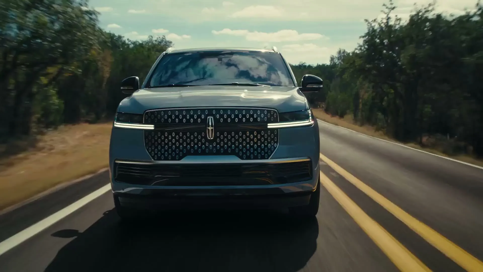 A Lincoln Navigator driving at dusk with its headlights lit