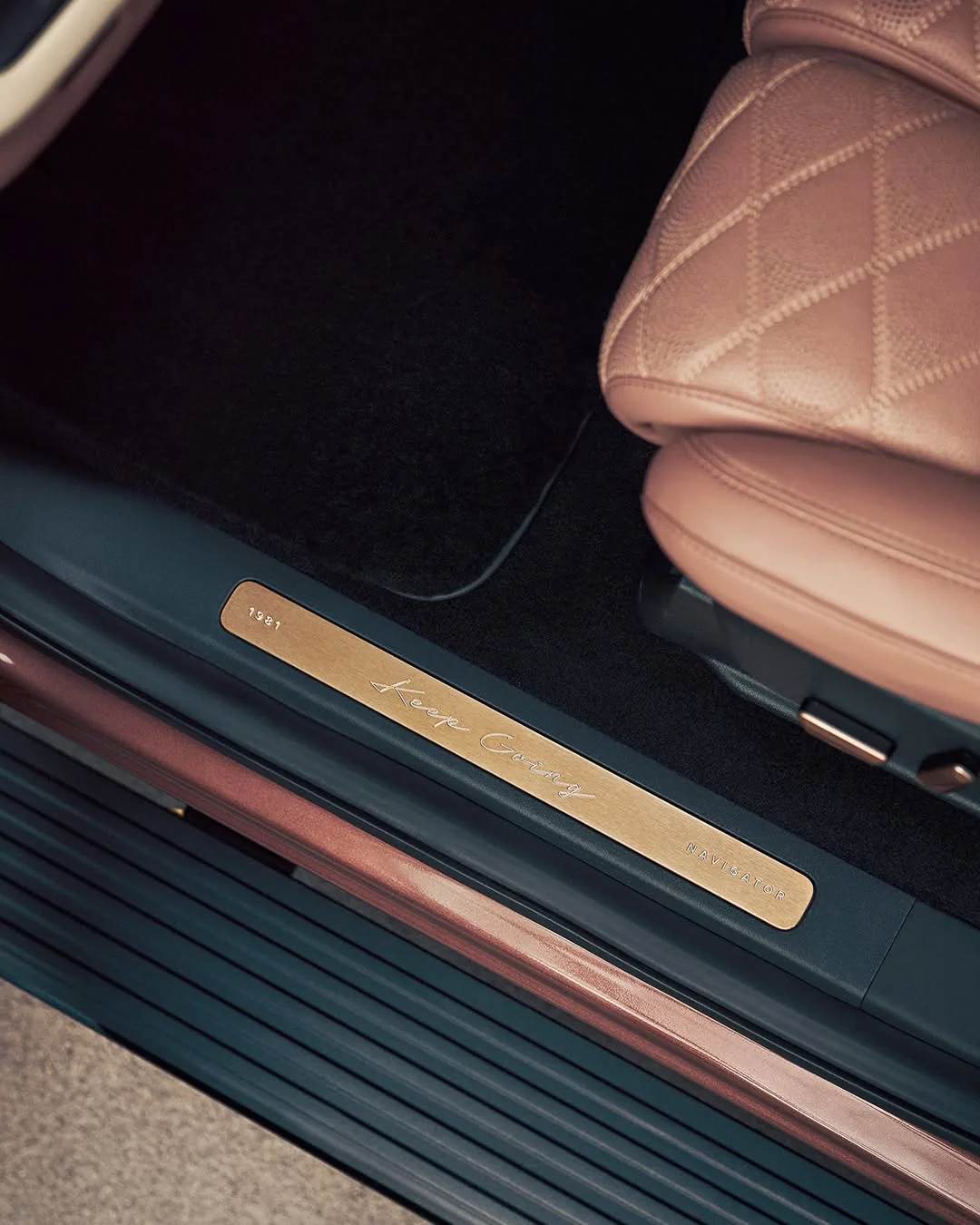 Brushed-gold door sill plate reading Keep Going and 1981 next to quilted rose leather