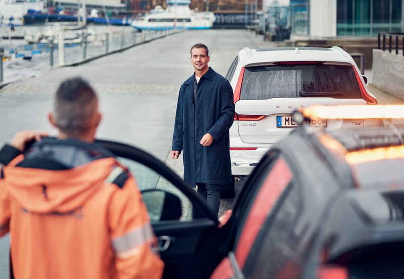 Volvo owner standing beside their disabled vehicle on the roadside, waiting for a tow truck as part of Volvo Roadside Assistance Plus service