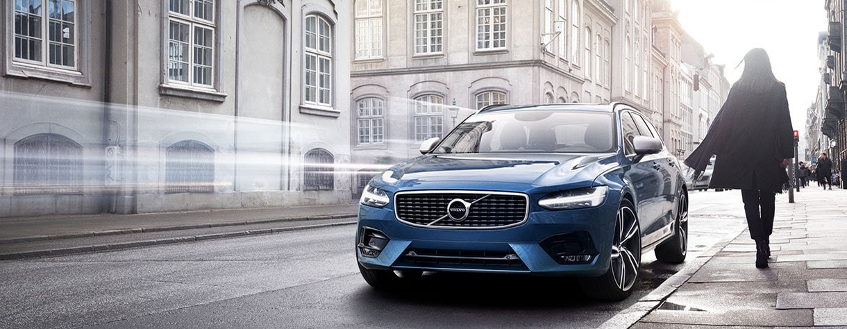 woman in city next to blue volvo