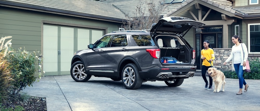 A family beside the open trunk of a gray Ford SUV outside a home