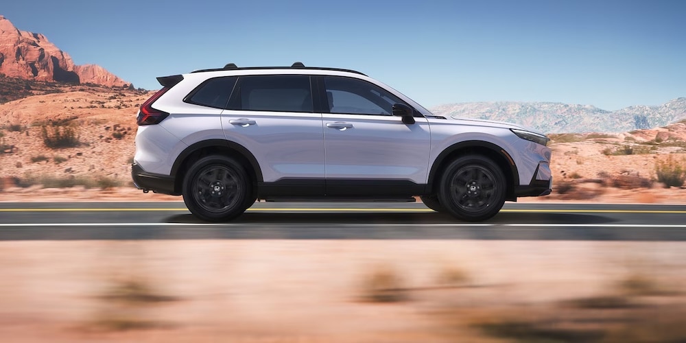 A side view of a white 2027 Honda CR-V SUV driving down a desert road