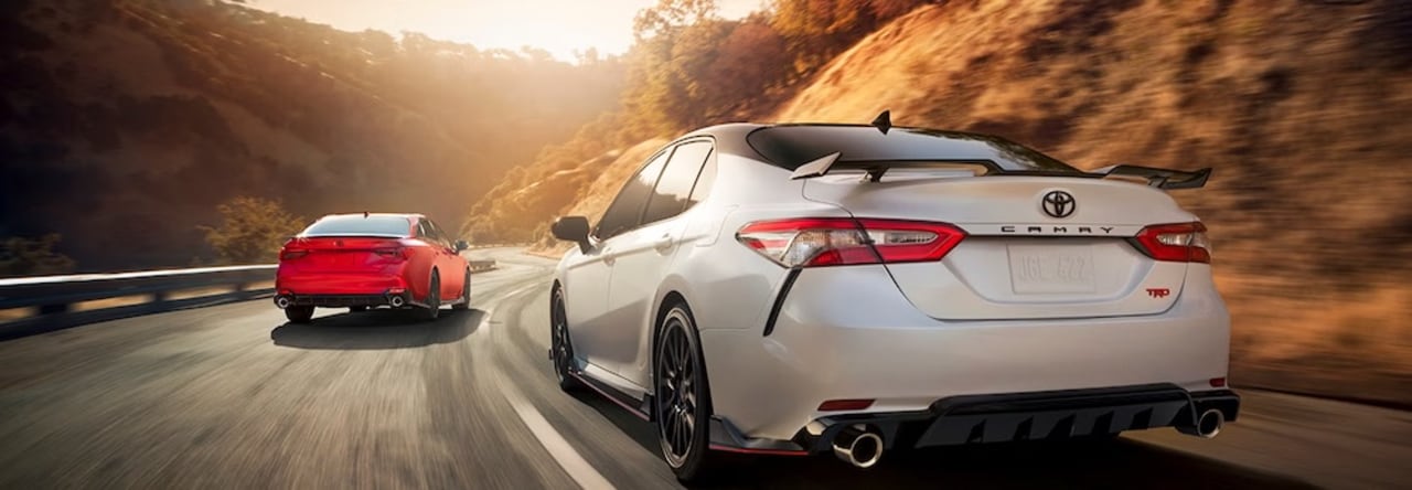 Two Toyota sedans, one red and one white, driving down a mountain road