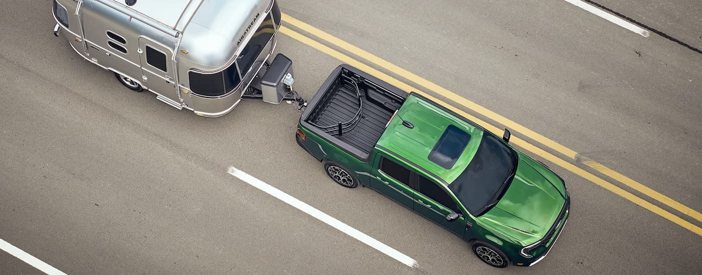 Green 2025 Ford Maverick towing a silver camper on a highway