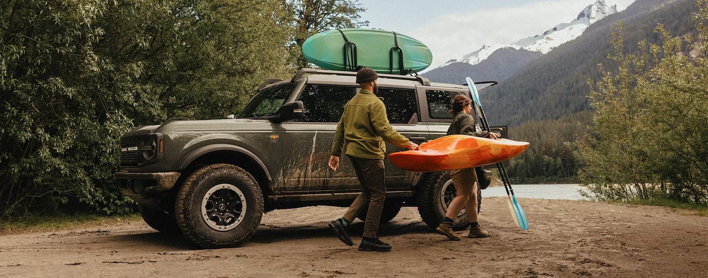 Two people carrying a kayak next to a green 2026 Ford Bronco