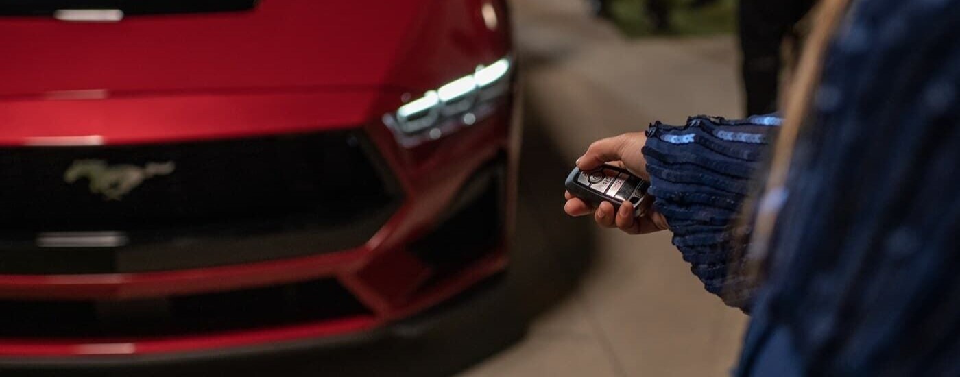 A person holding a keyfob next to a red 2024 Ford Mustang