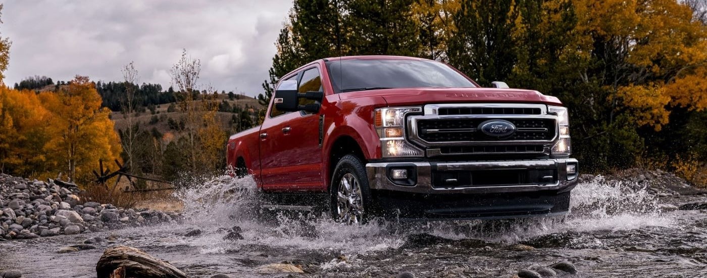 Red used 2021 Ford F-250 for sale driving over a shallow river.