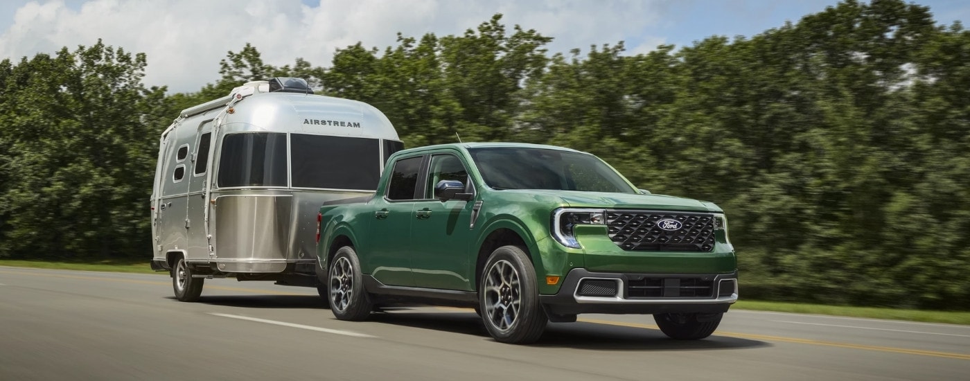 A green 2025 Ford Maverick from the front while towing a trailer after leaving a Ford dealer.