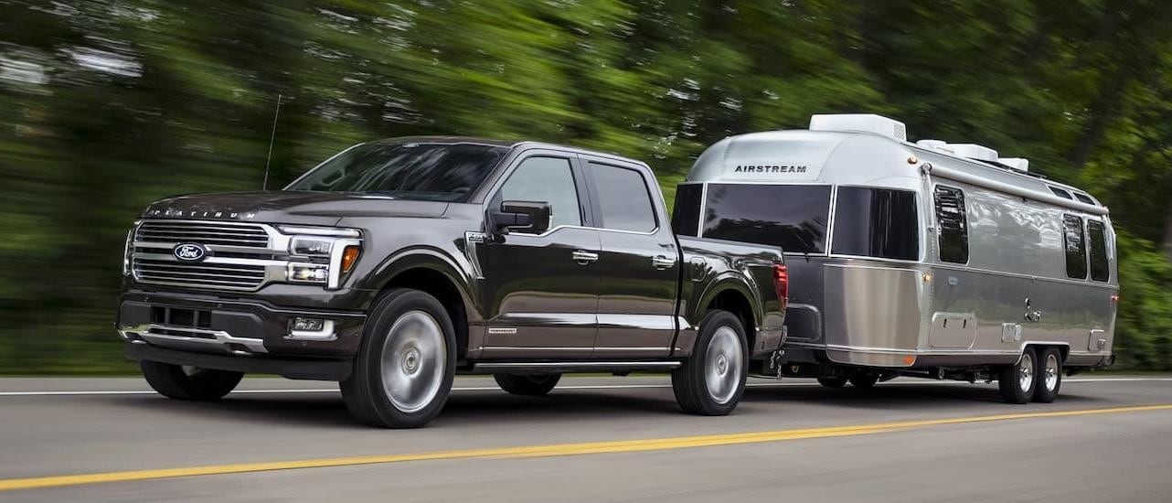 A grey 2025 Ford F-150 from the front at an angle while towing a camper.