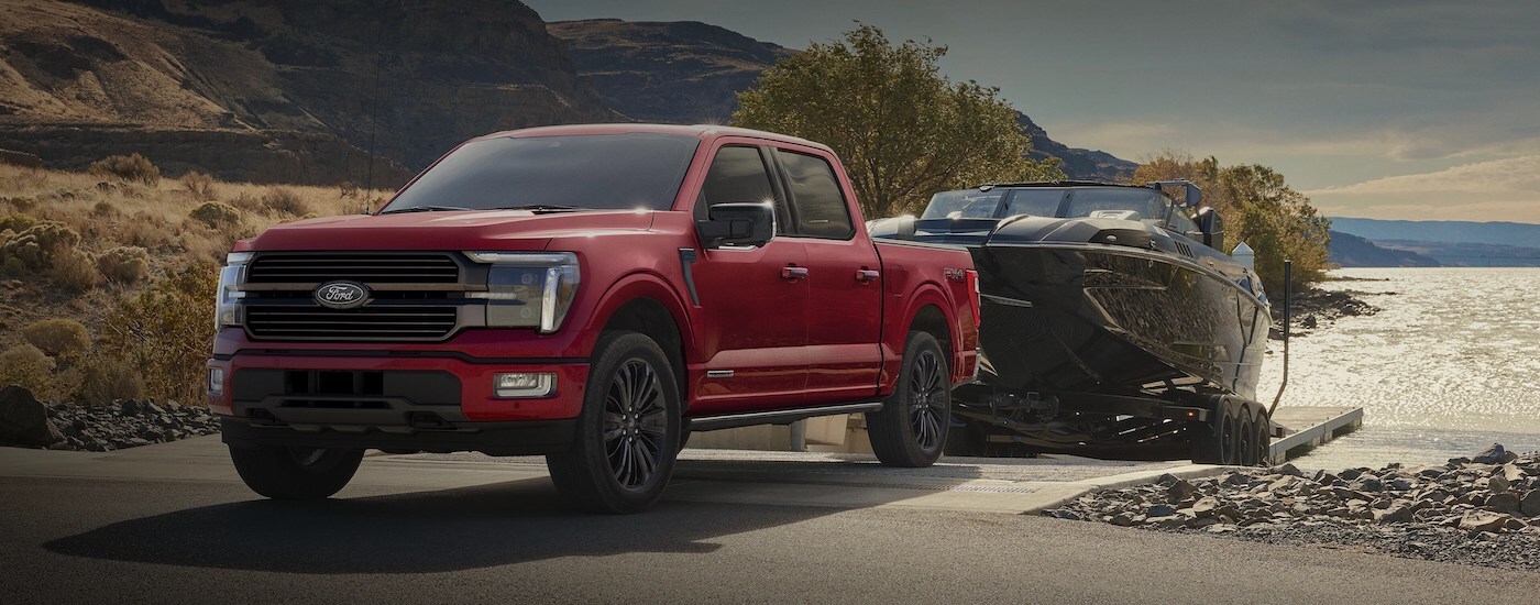 Red 2025 Ford F-150 STX towing a boat out of a lake.
