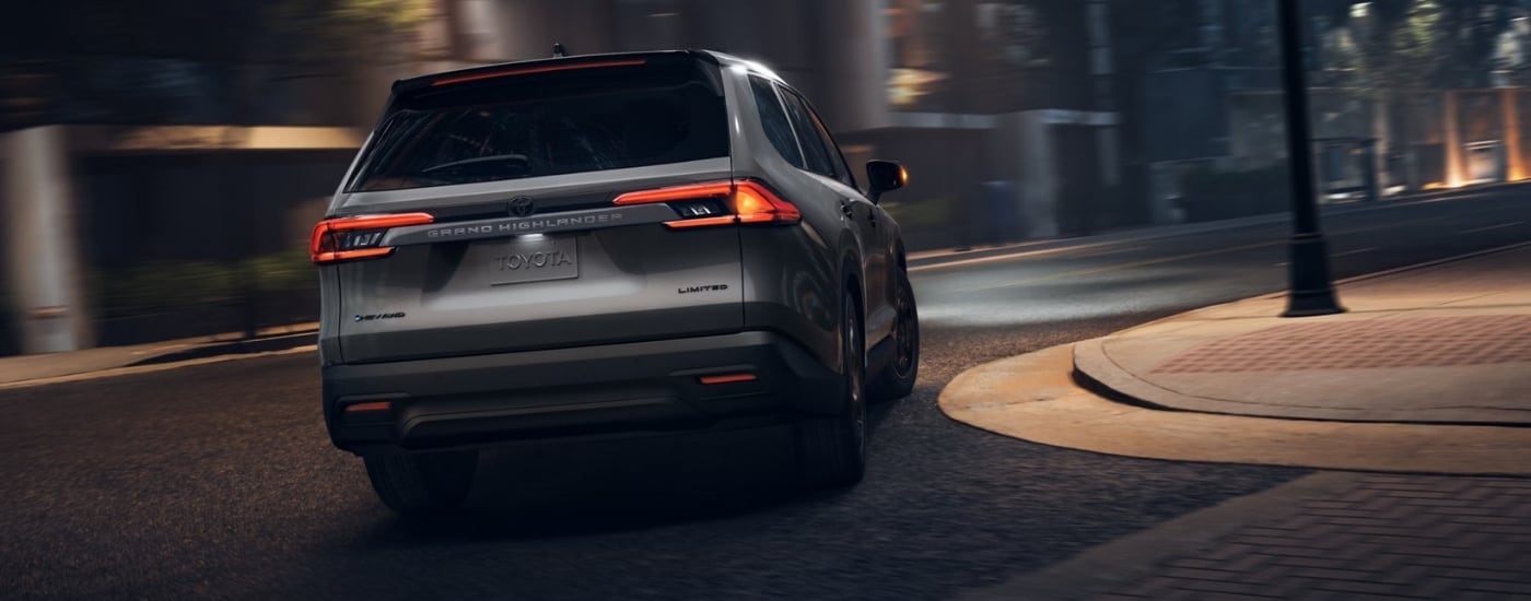 A silver 2025 Toyota Grand Highlander from the rear while rounding a bend.